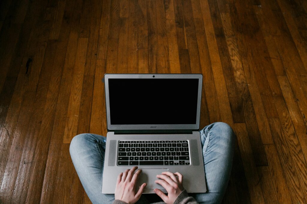 Person sitting cross-legged on hardwood floor using a laptop, focusing on minimalism.